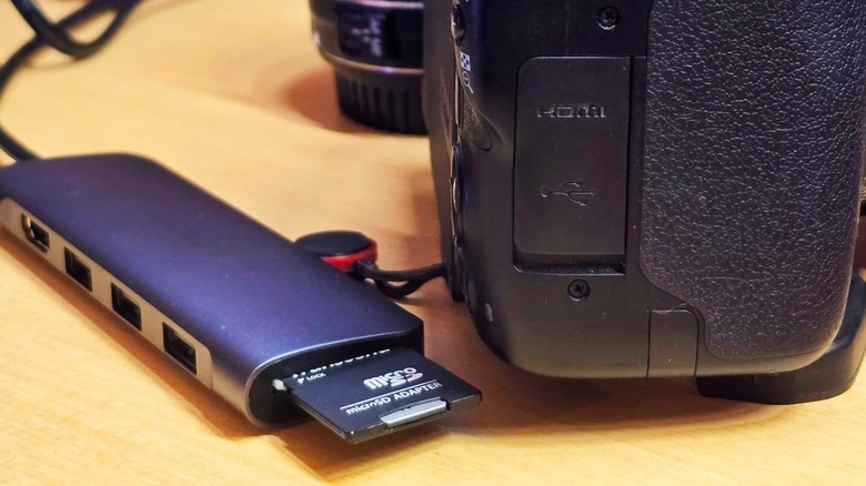 A multi-port USB hub with an SD card inserted, placed next to a digital camera.