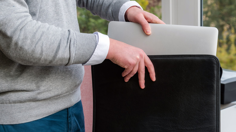 A man carefully sliding a laptop into a backpack compartment.