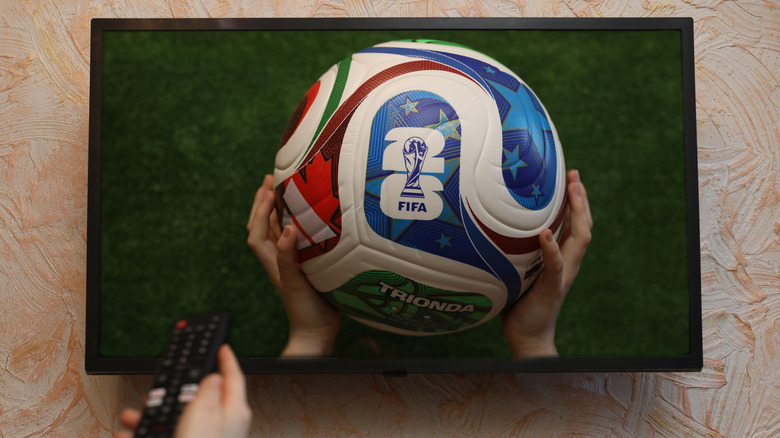 A person holding a remote control pointed at a TV screen showing a soccer match.