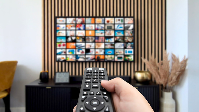 A person pointing a remote at a wall-mounted 65-inch TV screen.