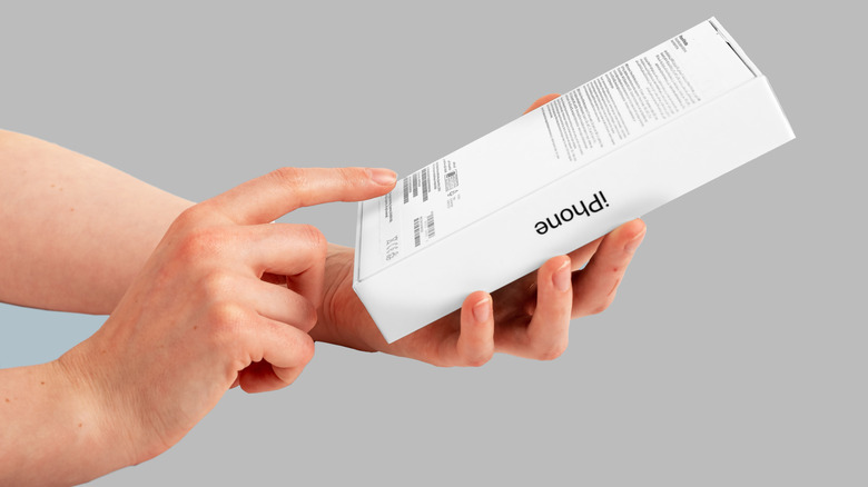 A person checking the back of an original iPhone retail box for printed serial and IMEI numbers.