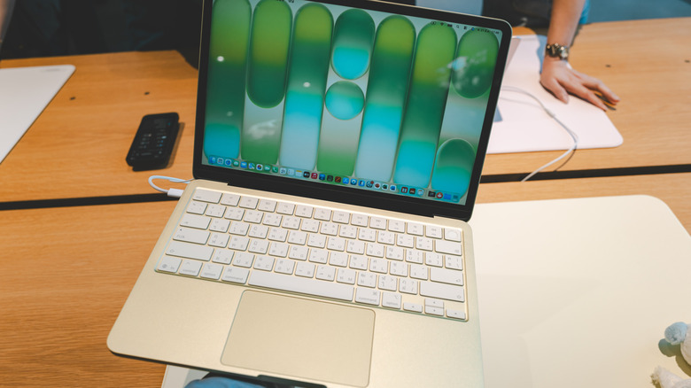 A person holding a compact laptop in a modern retail setting, suggesting the portability and form factor of a MacBook Neo competitor.