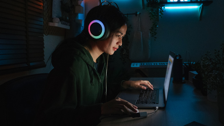 A woman wearing a gaming headset smiling while playing a game on her laptop.