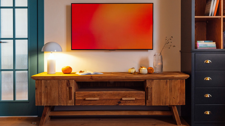 A wall-mounted TV with a red screen centered over a dark wood TV stand in a modern living room.