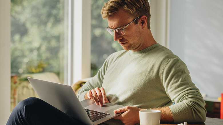 A man sitting comfortably at a table while using a laptop to manage his privacy settings.