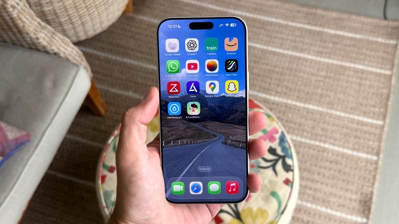 A close-up of a hand holding an iPhone with a bezel-less OLED screen.