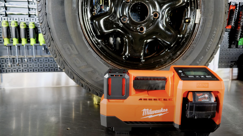 Milwaukee M18 tire inflator placed on the ground in front of a modern vehicle.