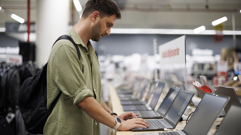 A male shopper in a tech store testing a laptop on a display shelf.