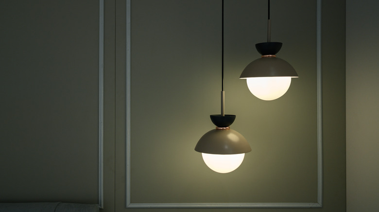 Two stylish hanging lamps with warm light bulbs set against a dark green wall.