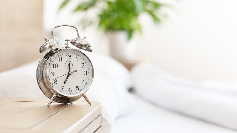 An analog alarm clock placed prominently on a bedside table in a clean bedroom.
