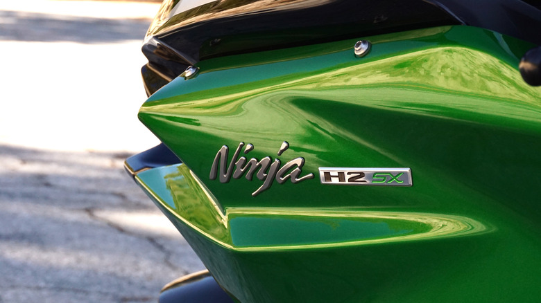 Close-up of the Ninja H2 SX emblem and supercharger branding on the motorcycle fairing.